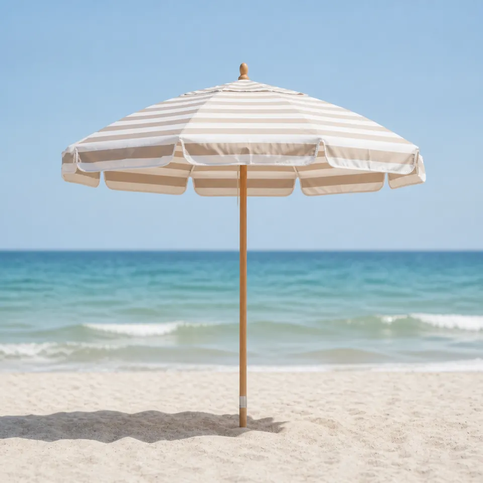 Traditional striped beach umbrella anchored in sand beside the ocean